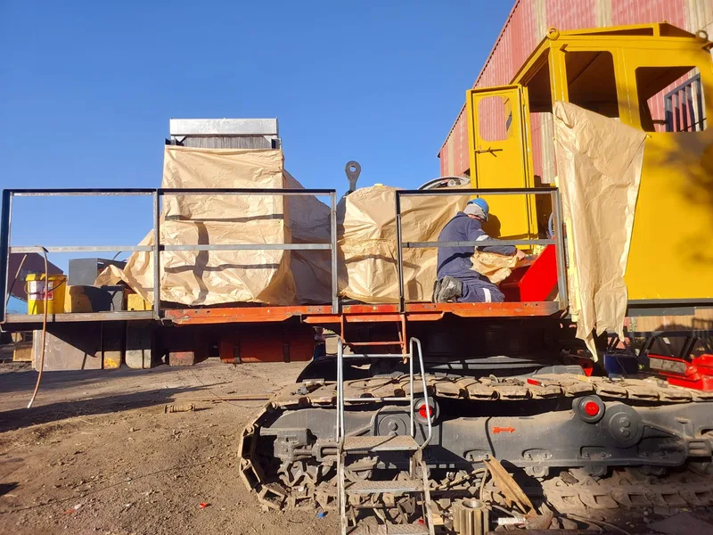 Yellow Bucyrus tracked crane during assembly beside a workshop.