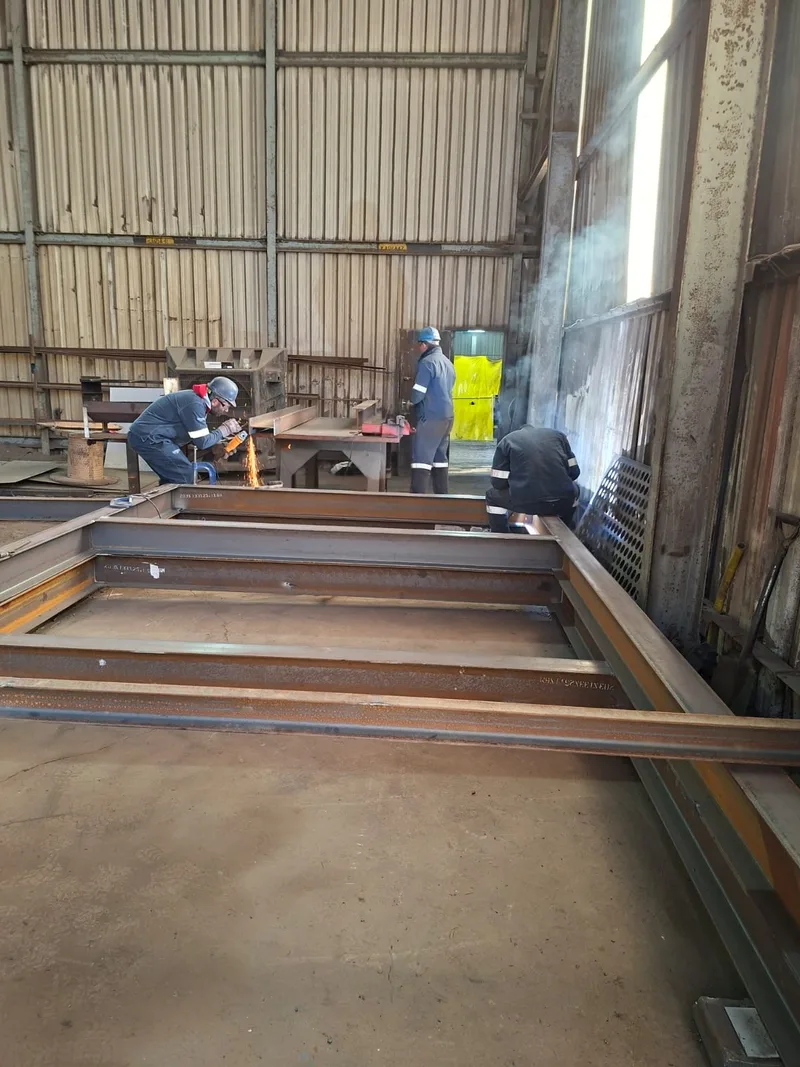 People working on a rectangular steel frame inside a workshop.