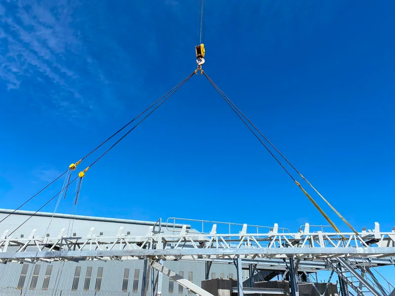 Chains and slings supporting a long steel conveyor section.